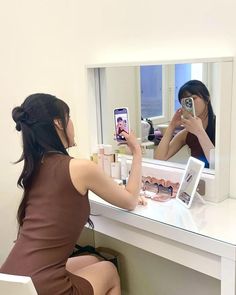 a woman sitting at a desk taking a selfie in front of a mirror with her cell phone