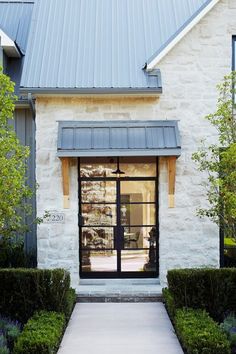 the front entrance to a white brick house with black glass doors and trimmed hedges on either side