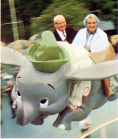 an older man and woman riding on the back of an elephant ride at a carnival