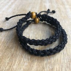 two black braided bracelets sitting on top of a wooden table