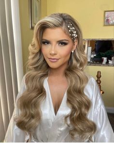 a woman with long blonde hair wearing a white blouse and pearls in her hair is looking at the camera