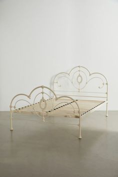 a white metal bed frame sitting on top of a cement floor next to a wall