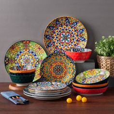 a table topped with lots of colorful plates and bowls next to a plant on top of a wooden table