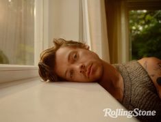 a man with tattoos laying down on a window sill looking at the camera while wearing a sweater