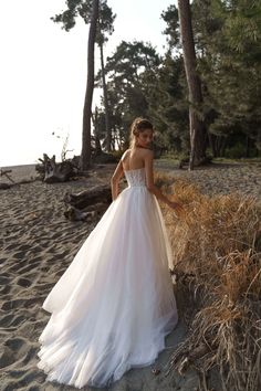 a woman standing on top of a sandy beach next to tall grass and pine trees