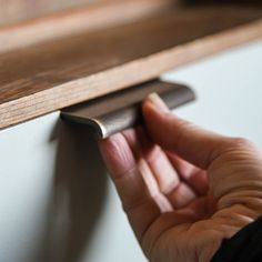 a person is holding onto the edge of a shelf with a metal handle on it