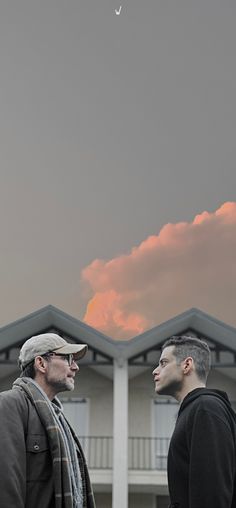 two men standing in front of a building with a kite flying above them and the sky behind them