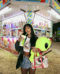 a woman standing in front of a food stand holding a drink and a stuffed animal