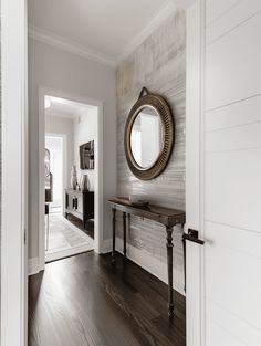 an entryway with a mirror and wooden flooring in the hallway leading to another room