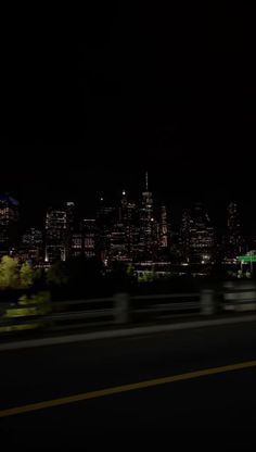 the city skyline is lit up at night with bright lights in the foreground and blurry cars on the road below