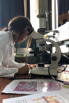 a woman sitting at a table in front of a microscope looking through the papers she is using