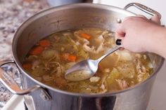 a person stirring a pot of soup with a spoon