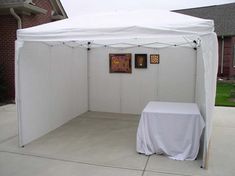 a white tent sitting on top of a sidewalk next to a wall with pictures on it