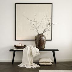 a vase sitting on top of a wooden table next to a white blanket and pillow