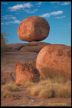 three large rocks sitting on top of a dry grass covered field with blue sky in the background