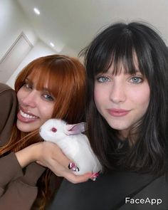 two beautiful young women posing for a photo with a white rabbit in their lap and one holding it up to the camera