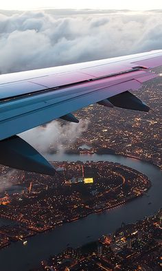 the wing of an airplane flying over a city at night with clouds in the sky