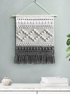 a crocheted wall hanging next to a potted plant on a white dresser