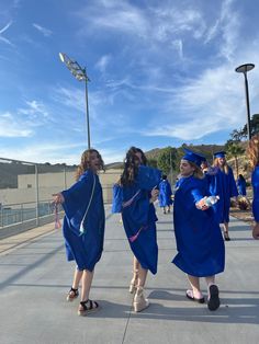 three girls in blue graduation gowns walk down the street