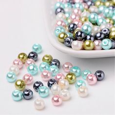 several different colored pearls in a white bowl next to a plate full of one pearl