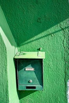 a green wall with a mailbox mounted to it's side and a shadow cast on the wall