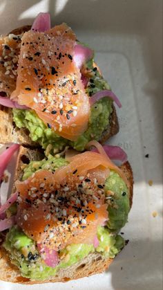 two sandwiches with salmon, lettuce and onions on them in a paper container