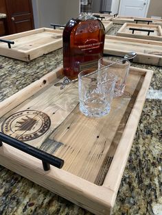 a wooden tray with two glasses and a bottle on it sitting on top of a counter