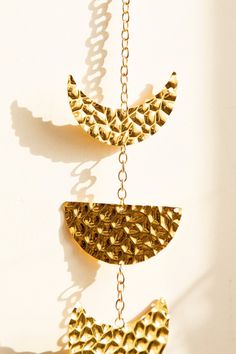 two gold necklaces hanging from chains on a white wall