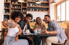 four people sitting at a table taking a selfie with their cell phone in a coffee shop