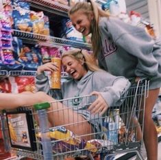 two young women are laughing while pushing a shopping cart in a grocery store with drinks and snacks