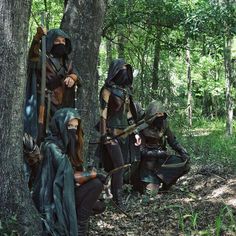 three people dressed up in costume standing next to each other near a tree trunk and some trees