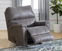 a grey recliner chair sitting on top of a rug next to a potted plant