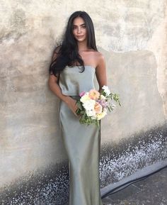 a woman standing next to a wall holding a bouquet