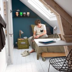 a young man sitting on top of a bed next to a desk in a loft