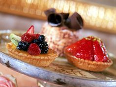 two desserts are on a silver tray with flowers and roses around the edge, one is topped with berries