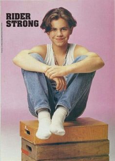 a young man sitting on top of a wooden box with his legs crossed and smiling