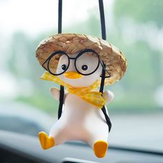 a toy penguin wearing glasses and a straw hat hanging from a car dash board holder