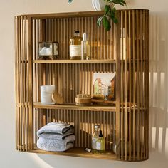 a bamboo shelf with towels, soaps and other items on it in front of a white wall