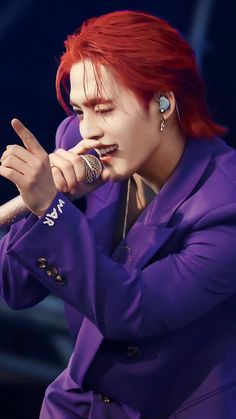 a person with red hair and piercings holding a microphone in their hand while wearing a purple suit