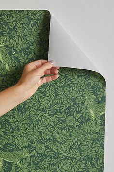 a person's hand on top of a green and white wallpaper with an animal pattern