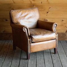 a brown leather chair sitting on top of a wooden floor next to a wood wall