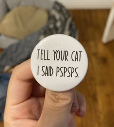 a person holding a white button that says tell your cat i said pspps