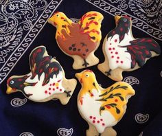 four decorated cookies in the shape of roosters on a blue and white table cloth