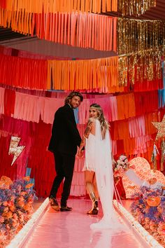 a bride and groom are standing in front of colorful streamers on the wall behind them