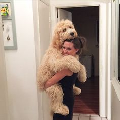 a woman holding a dog in her arms while standing next to a doorway with the door open