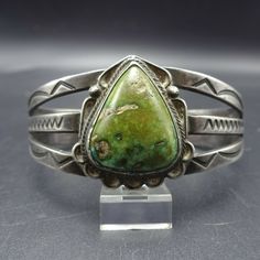 "VINTAGE NAVAJO BRACELET DESCRIPTION: This spectacular bracelet features an abundance of hand applied stamp-work on the split cuff. A gorgeous green cab of natural turquoise is at the center. This bracelet will be a cherished addition to your collection of fine vintage Native American jewelry. MEASUREMENTS: Interior of the cuff measures 5 3/4\" with an additional 7/8\" slightly adjustable gap. Total circumference: 6 5/8\" Measures 2 3/8\" straight across the widest part (from wrist bone to wrist Southwestern Engraved Green Jewelry, Southwestern Style Engraved Green Jewelry, Artisan Green Bangle Jewelry, Green Bohemian Bracelets With Patina, Artisan Green Cuff Bangle Bracelet, Vintage Green Bracelet With Patina, Southwestern Green Bangle Jewelry, Adjustable Southwestern Green Cuff Bracelet, Southwestern Style Green Bangle Jewelry