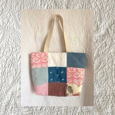 a patchwork tote bag hanging on a white quilted bed cover with pink, blue and brown accents