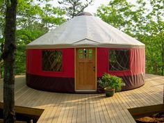 a red and white yurt sitting on top of a wooden deck next to trees