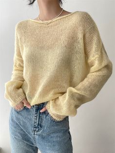 a woman wearing a yellow sweater and jeans standing in front of a white wall with her hands on her hips