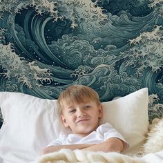 a young boy laying on top of a bed under a blue and white wallpaper